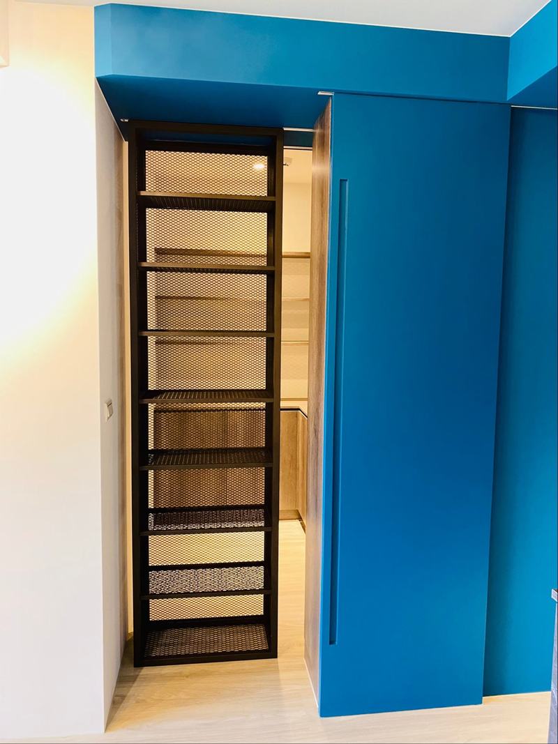 隱藏在深藍推門後方的金屬網格書櫃，兼具展示與收納機能，為空間增添工業風的俐落感。
